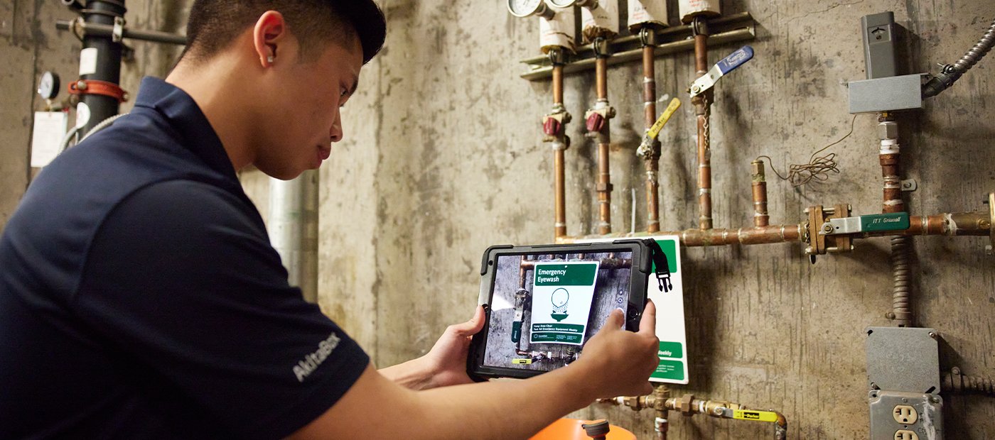A worker points a tablet at a building asset during a facility condition assessment.