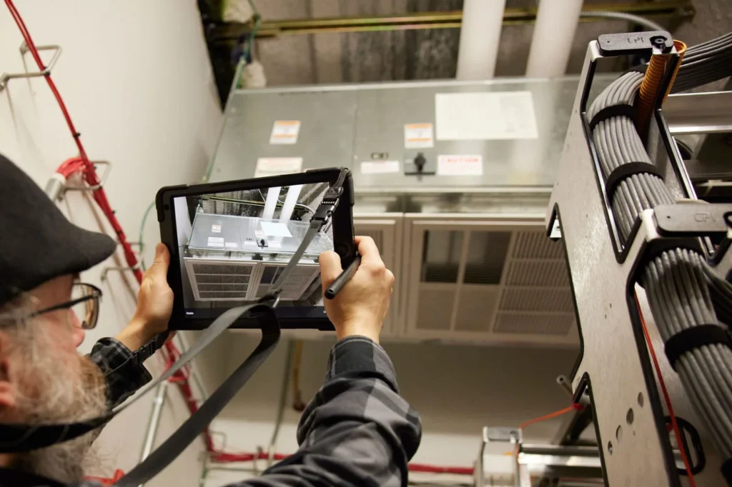 A person points a tablet at an HVAC until to take a photo for facility asset data collection.