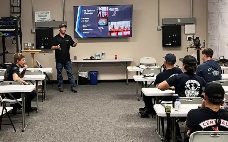 Instructor leads a fire-safety training in a classroom, presenting slides on a screen to seated students at desks.