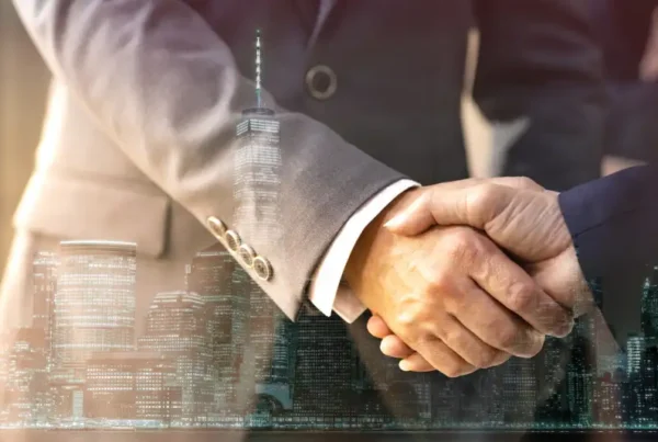 Handshake between two professionals overlaid with a city skyline, symbolizing a business deal.