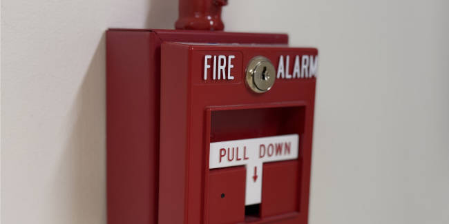 Red wall-mounted fire alarm pull station with a white 'PULL DOWN' label and a small credit lock above it