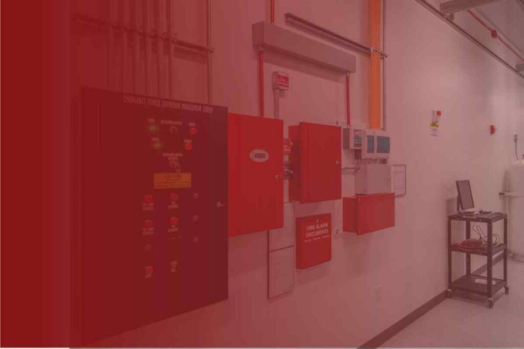 Industrial corridor with red fire alarm control panels on the wall and a small wheeled workstation cart to the right.
